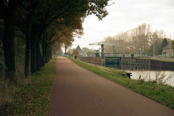 荷兰黑尔蒙市绿树旁一条自行车道和一条河流的风景 — 图库照片