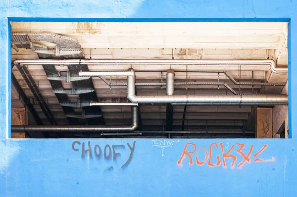 Grafiti Yazıları Ile Mavi Bir Duvarın Açılışından Görülen Bir Boru — Stok fotoğraf