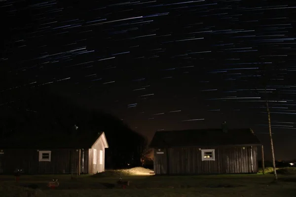 A long exposure shot of starts in the sky during nighttime with two small cottages below