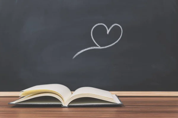 An open book and and heart shape on the blackboard background