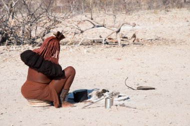 Himba kabilesinden bir kadın Namibya 'da güneşin altında oturuyor.
