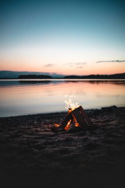 Gün batımında gölün kıyısında yanan bir şenlik ateşinin dikey çekimi.