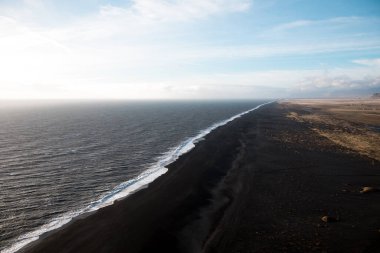 Mavi ama bulutlu gökyüzünün altında İzlanda 'da siyah kumlu kıyı şeridi