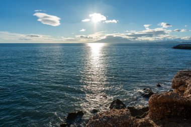 Güneşli bir günde mavi bulutlu gökyüzüne karşı kumsalda ve deniz manzaralı güzel bir kayalık.