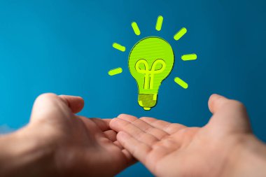 Bir insanın ellerinin üzerinde havada süzülen 3 boyutlu yeşil bir ampul.