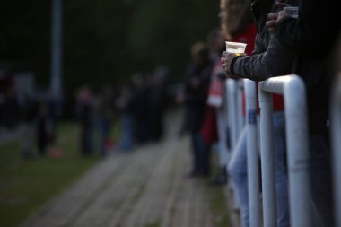 Elinde plastik bir bardak tutan ve spor müsabakalarını izleyen bir seyirci - boşluğu kopyala