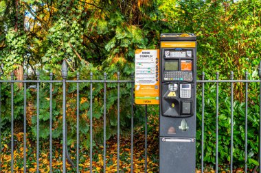 Flowbird marka bir Fransız parkmetresi arka planda metalik bir çitin yanında..