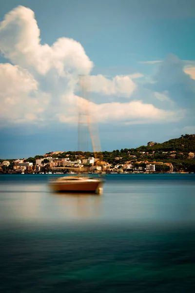 A vertical photo of a lake, a boat and buildings on a forest hill in Geneva City in Switzerland