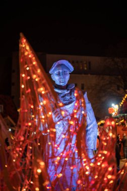 Arka planda bir heykel olan turuncu Noel ışıklarının dikey yakın çekimi. Dortmund Noel Pazarı.
