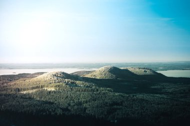 Güneşli bir günde kışın ormanlarla kaplı karlı tepelerin kuş bakışı görüntüsü.