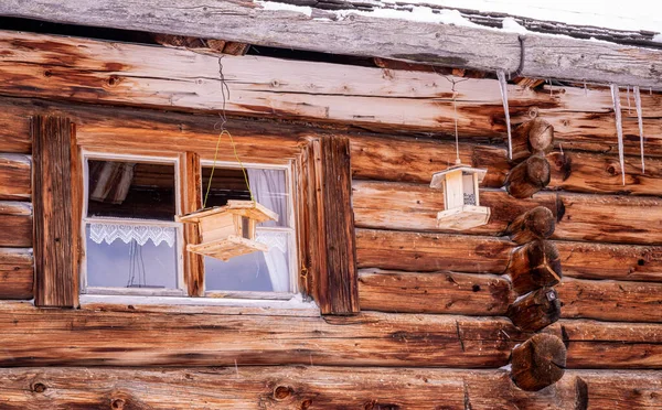 A beautiful shot of an old wooden house with bird feeders and falling snow and a small window