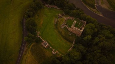 Northumberland 'da yoğun yeşil ağaçlarla çevrili eski bir kalenin havadan çekilmiş görüntüsü.