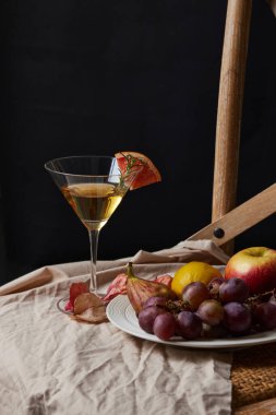 Alkollü bir içecek ve kırışık bir bez üzerindeki meyve tabağının dikey fotoğrafı ve siyah bir arka plan.