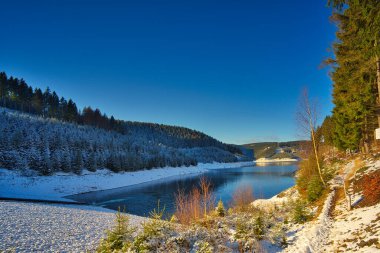 Almanya 'nın Thüringen Ormanı' ndaki Goldistal rezervuarında güzel bir karlı göl manzarası.