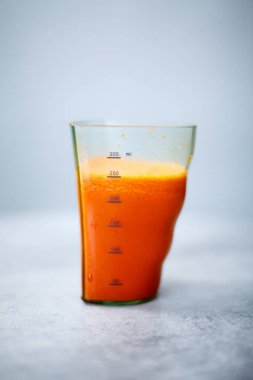 Meyve sıkacağı kabındaki taze havuç suyunun dikey izole edilmiş görüntüsü.