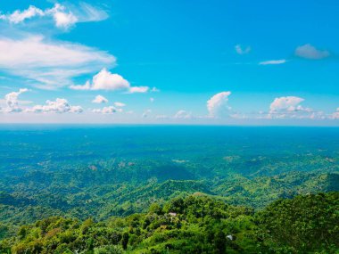Bulutlu mavi gökyüzünün altında parlayan yeşil dağların hava manzarası.