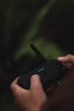 Bir adamın dikey yakın plan görüntüsü bir ormanın bulanık arka planına sahip uzaktan kumandalı drone kullanıyor.