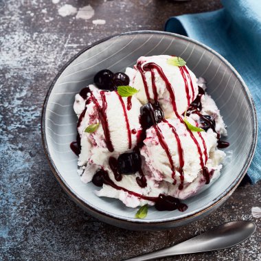 Vişneli ve nane yapraklarıyla süslenmiş, vişneli ve şuruplu vanilyalı dondurma manzarası.