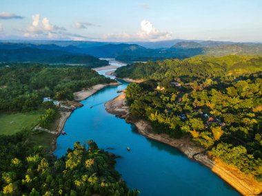 Bulutlu mavi gökyüzünün altında yeşilliklerle çevrili akan nehrin hava manzarası.