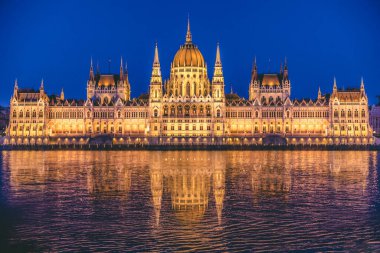 Macar parlamento binasının alacakaranlıkta ışıklarla aydınlatılmış manzarası suya yansıyor.