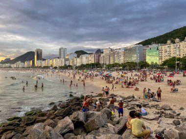 Gün batımı, Copacabana 'nın kayaları, plajları ve binalarını dramatik mavi bulutlarla aydınlatıyor. Dramatik altında yuvarlanan dalga