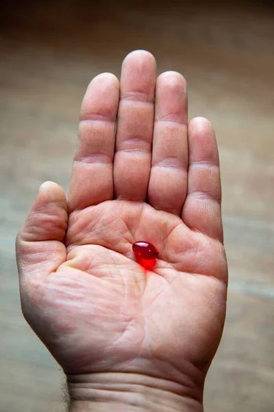 One Hand Takes Red Pill Wooden Background Closeup — Stock Photo, Image