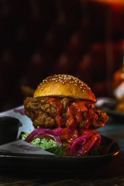 Koyu, pis bir restoranda tavuk burgerinin dikey çekimi.