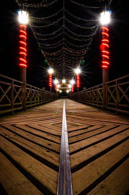 Geceleri gölün kıyısındaki aydınlatılmış bir iskelenin dikey görüntüsü.