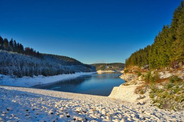 Almanya 'nın Thüringen Ormanı' ndaki Goldistal rezervuarında güzel bir karlı göl manzarası.