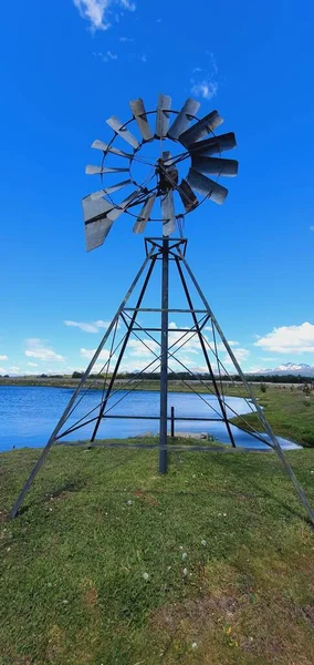 青い空の下の湖に対して草の上に古いヴィンテージの風車の垂直方向の眺め — ストック写真