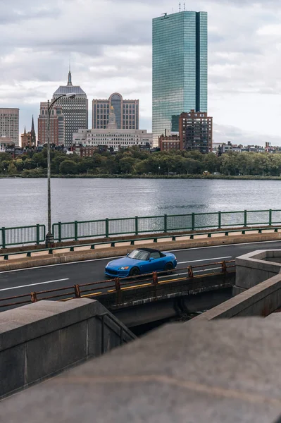 ボストン市のスカイラインの前を走る青い車の垂直ショット — ストック写真