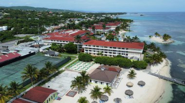 An aerial of hotels on a beach covered with greenery against a turquoise sea in Montego Bay, Jamaica clipart