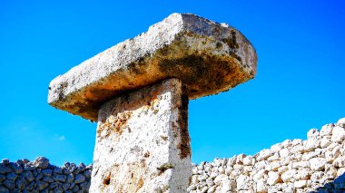 Mavi gökyüzü arka planında taşlı bir arkeolojik alanın manzarası.