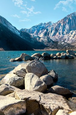 Sahildeki devasa taşların dikey çekimi. Arka planda dağlar var.