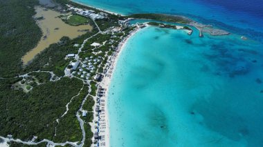 Kumsalda turkuaz bir denize karşı yeşillikle kaplı otellerin kuş bakışı görüntüsü.