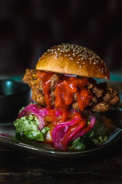 Koyu, pis bir restoranda tavuk burgerinin dikey çekimi.