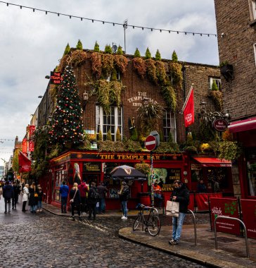 Sokağın köşesindeki Tapınak Bar 'da Noel süsleri ve yağmurlu bir öğleden sonra Dublin' de insanlar sokakta dikiliyor.