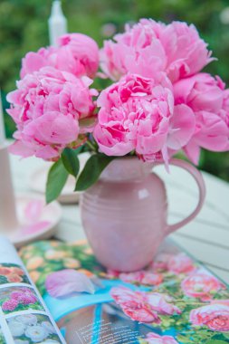 Açık bir kitabın üstündeki vazoda güzel pembe şakayıkların dikey görüntüsü.