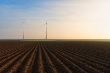 Gün batımında bulutlu gökyüzünün altında büyük bir tarlada güzel bir rüzgar değirmeni görüntüsü.