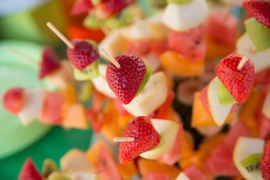 Tahta çubuklarda dilimlenmiş çilek, kivi ve muz resmi.