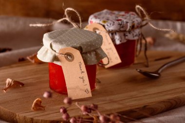 Tekstil kapaklı küçük cam kavanozlarda reçel, küçük etiketler, kaşık, kuru yapraklar ve tahta tepside çiçekler.