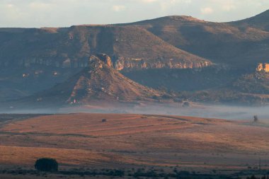 Bulutlu gökyüzüne ve sisli vadilere karşı kayalık tepeleri olan bir manzara.