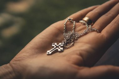 Altın yüzüklü, insan avucundaki zincirle gümüş haçın sığ odak noktası.