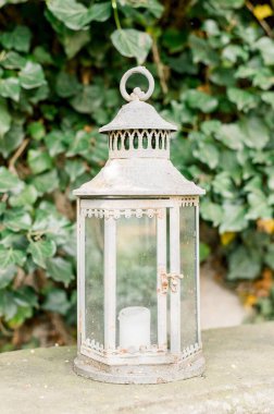 Güneşli bir günde, bahçesinde mum olan beyaz dekoratif bir fenerin dikey yakın çekimi.