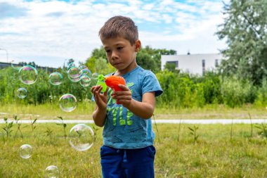 Tatlı Polonyalı beyaz bir çocuk güneşli bir günde dışarıda sabun köpüğü yaratıyor.