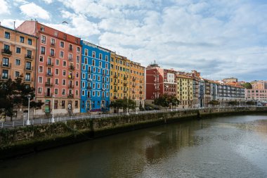 İspanya, Bilbao 'da bulutlu bir gökyüzüne karşı nehir kıyısındaki renkli binalar.