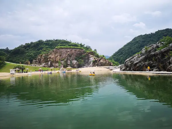 青い空の下の湖に反射する緑の岩山の下の人々の風景 — ストック写真