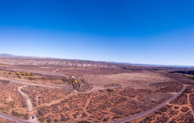 Arkasında bulutsuz bir gökyüzü olan ıssız bir bölgeden geçen bir yolun hava görüntüsü.