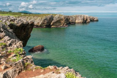 Mavi bulutlu gökyüzünün altındaki uçurumlarla çevrili sakin bir okyanus.