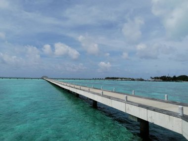Maldivler 'de mavi gökyüzünün altında sakin deniz suyunun üzerinde uzun beton bir köprü.